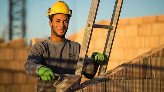 Ein Maurer steht auf der Leiter und hält eine Zementkelle in der Hand