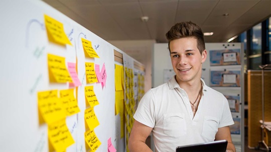 Ein Informatiker steht von der Projektwand mit Post-it Zetteln