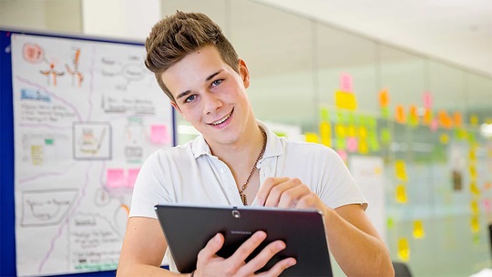 Ein Informatiker steht vor einem Flipchart und macht sich Notizen auf seinem Tablet