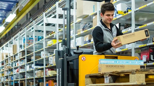 Ein Logistiker auf dem Gabelstapler hält ein Packet in der Hand