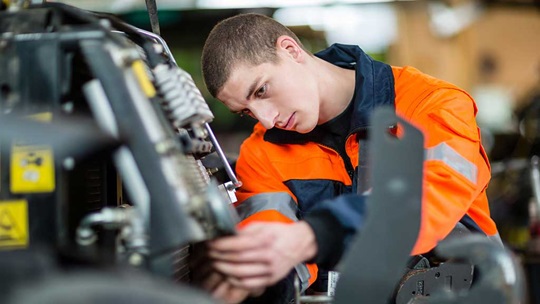 Ein Landmaschinenmechaniker schraubt am Motor eine Mutter fest
