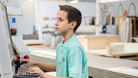 Ein Schreiner steht in der Werkstatt vor einem Computer