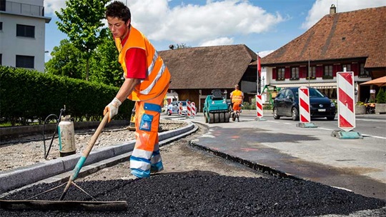Ein Strassenbauer verteilt mit einem Rechen den Teer