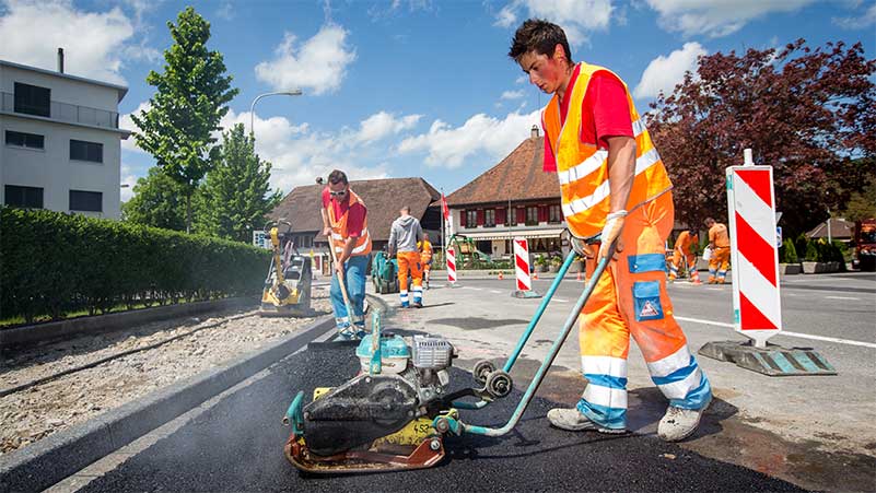 Ein Strassenbauer macht mit einer Walze den Teer fest