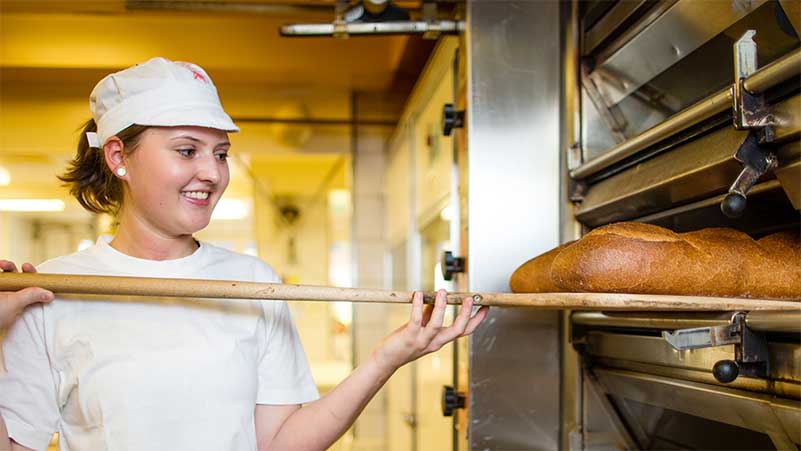 Eine Bäckerin nimmt Brotlaibe aus dem Ofen