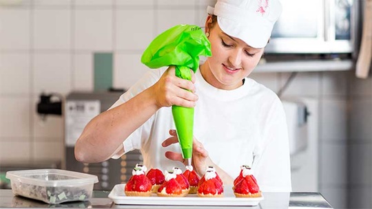 Eine Bäckerin dekoriert Erdbeertörtli mit Rahm