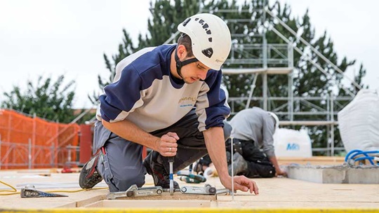 Ein Zimmermann montiert auf dem Dach erste Holzlatten