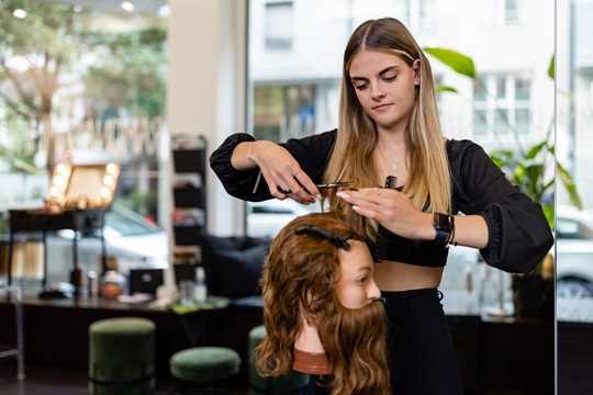 Eine Coiffeuse übt an einer Haarpuppe
