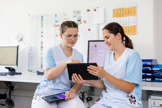Eine Fachfrau Gesundheit lässt sich am Tablet etwas erklären