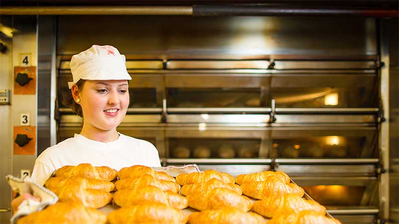 Eine Bäckerin nimmt Gipfeli auf einem Blech aus dem Ofen